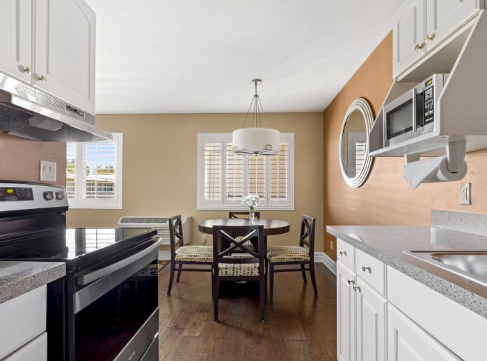 A modern kitchen with white cabinets, grey countertops, stainless steel appliances, and a dining area with a round table and four chairs.
