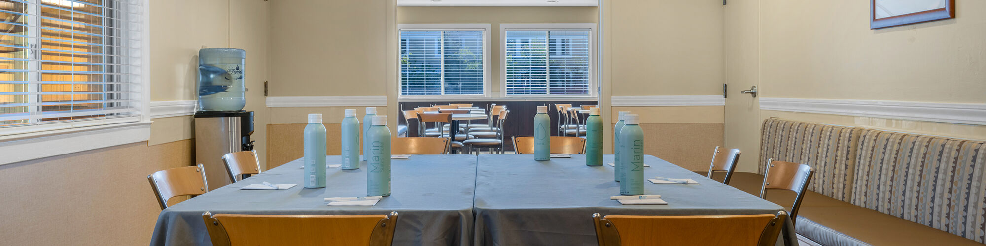 The image shows a small dining or meeting room with a table covered in a gray tablecloth, chairs around it, and bottles of water on the table.